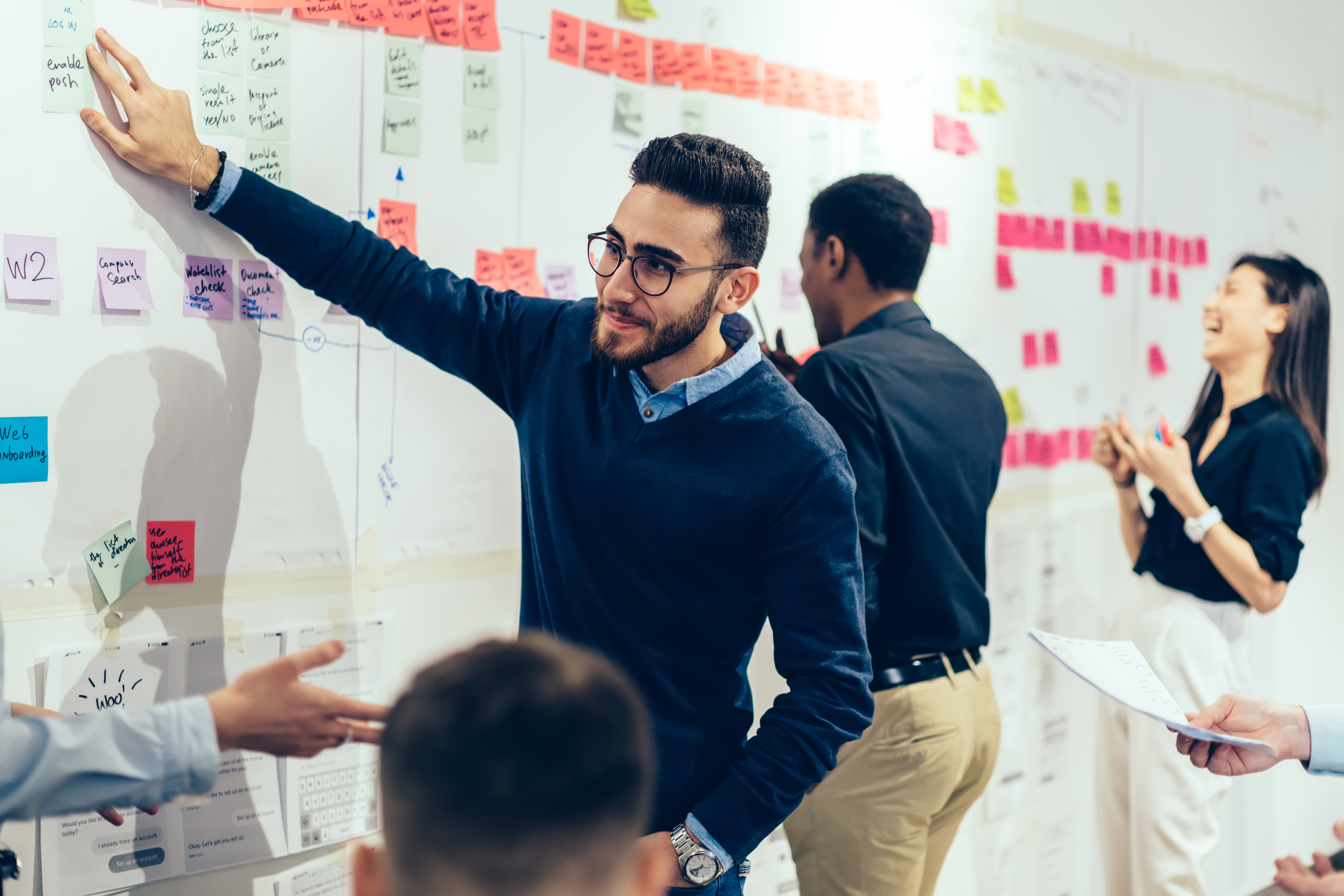 Smart multiethnic office employee making sticky notes on wall at office